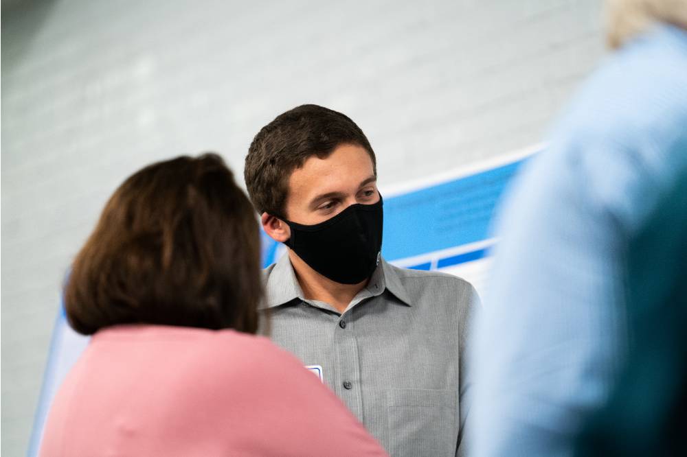 Scholar wearing mask giving poster presentation to a guest.